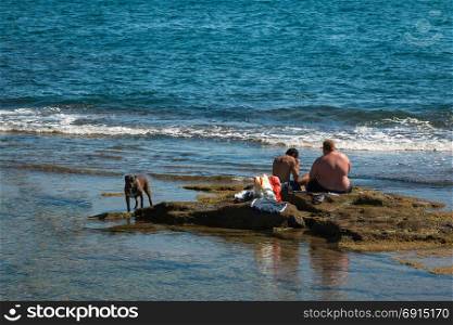 LIVORNO, ITALY - AUGUST 2015: Black Dog and Two Young Boys seated on Reef near Sea