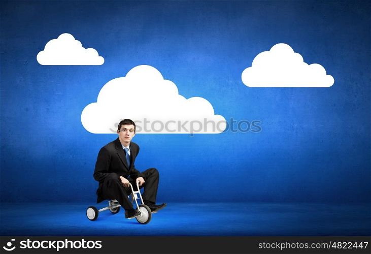 Lke a child. Young handsome businessman riding three wheeled bicycle