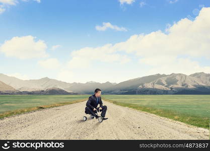 Lke a child. Young handsome businessman riding three wheeled bicycle