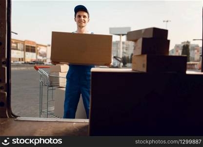 Loader in uniform holding carton box, delivery service. Man standing at cardboard packages in vehicle, male deliver, courier or shipping job. Loader in uniform holding box, delivery service