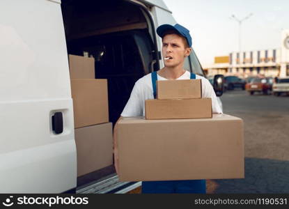 Loader in uniform holding stack of parcels, delivery service. Man standing at cardboard packages in vehicle, male deliver, courier or shipping job. Loader holding stack of parcels, delivery service