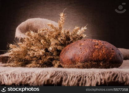 Loaf of bread and rye ears still life on rustic background