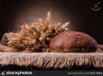 Loaf of bread and rye ears still life on rustic background