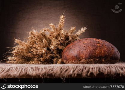 Loaf of bread and rye ears still life on rustic background