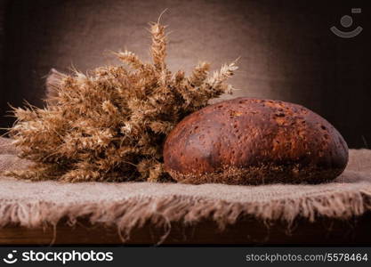 Loaf of bread and rye ears still life on rustic background