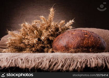 Loaf of bread and rye ears still life on rustic background