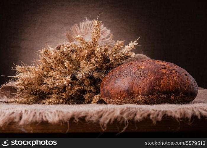 Loaf of bread and rye ears still life on rustic background