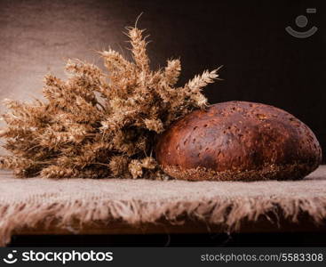 Loaf of bread and rye ears still life on rustic background