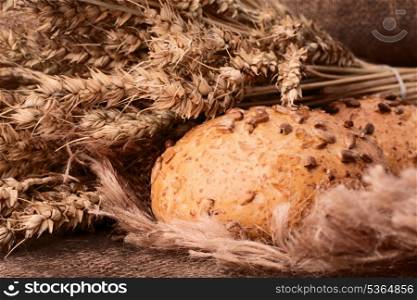 Loaf of bread and wheat ears still life on rustic background