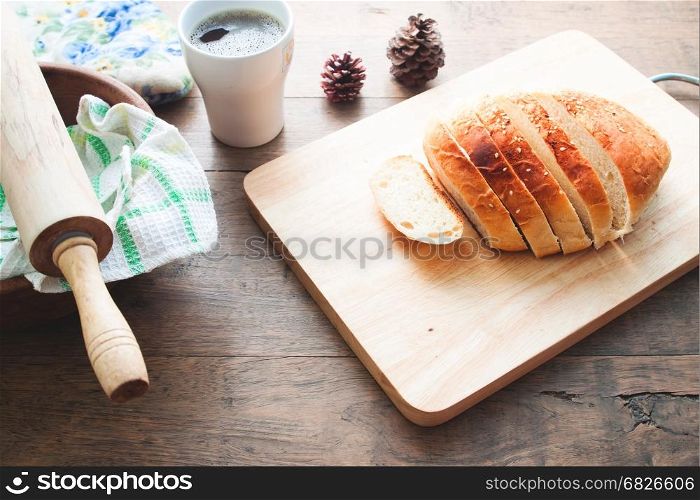 loaf of bread on wood background with cup of coffee and bakery tools, food closeup