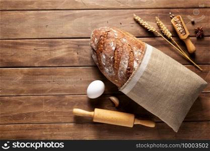 Loaf of fresh bread and bakery ingredients for homemade baking on wooden table. Baker food set at wood plank board background texture with copy space. Flat lay top view