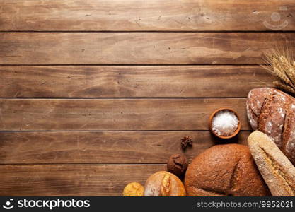 Loaf of fresh bread and buns on wooden table. Assortment of bakery food at wood plank board background texture with copy space. Flat lay top view
