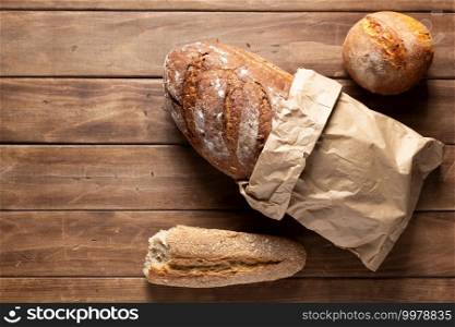 Loaf of fresh bread and buns on wooden table. Assortment of bakery food at wood plank board background texture with copy space. Flat lay top view