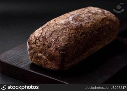 Loaf of fresh crispy brown bread with grains and seeds on dark concrete background