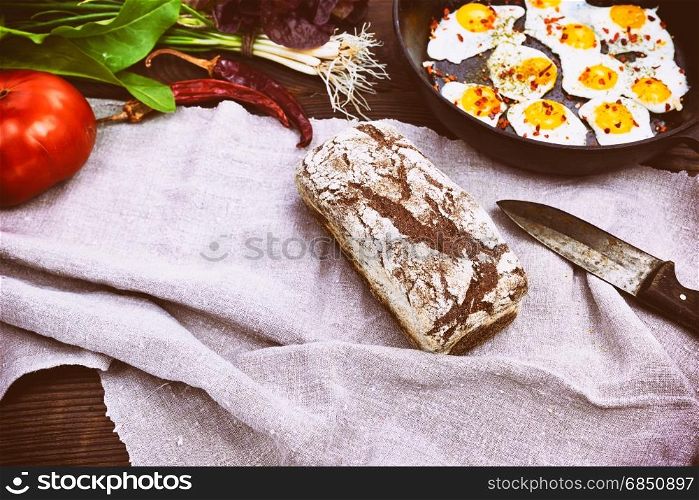 loaf of rye bread and fried eggs in a black frying pan, vintage toning