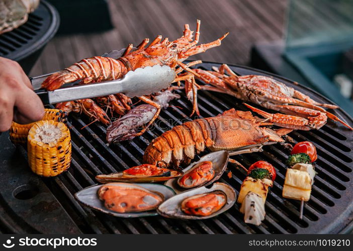 Lobster, rock lobster and mix seafood barbecue cokking on grill - seafood dinner party concept