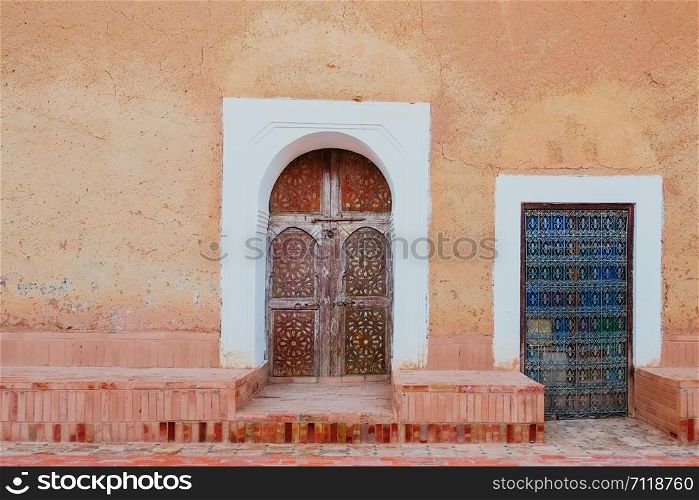 Local antique Moroccan pattern carved wooden doors against old orange pink wall.