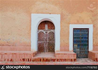 Local antique Moroccan pattern carved wooden doors against old orange pink wall.