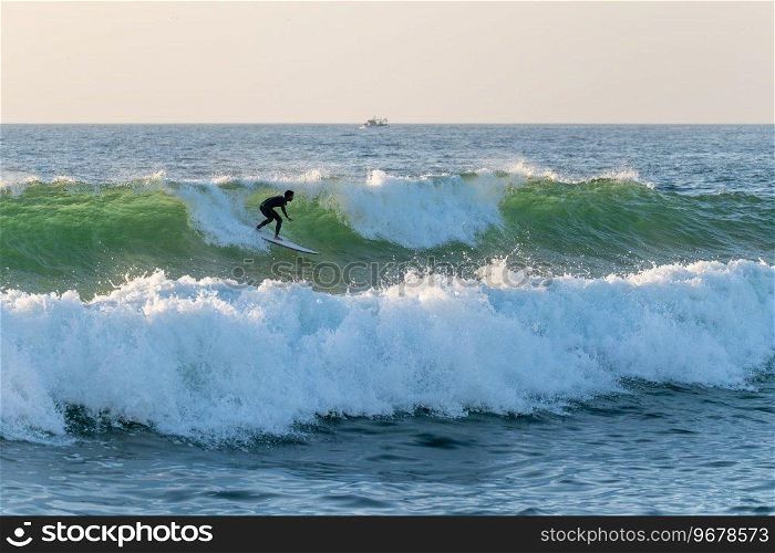 Local surfer riding waves with a short board in Furadouro beach, Portugal. Men catching waves in ocean. Surfing action water board sport.