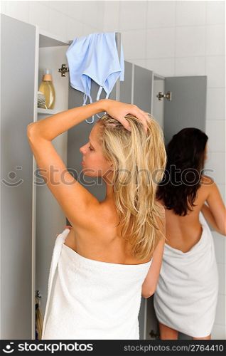 Locker room two relaxed women wrapped in towel going shower