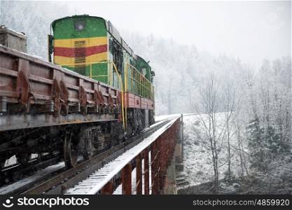 Locomotive of cargo on the bridge near winter forest with trees in snow