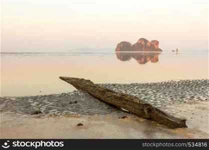 Log on beach and reflections of limestone islands, Hua Hin beach, Trang province, Thailand