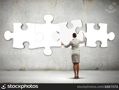 Logic thinking. Rear view of businesswoman connecting white puzzle