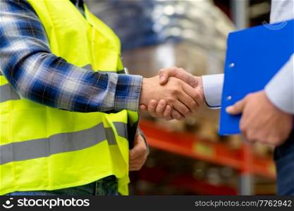 logistic business and cooperation concept - close up of manual worker and businessman with clipboard shaking hands and making deal at warehouse. worker and businessman shaking hands at warehouse