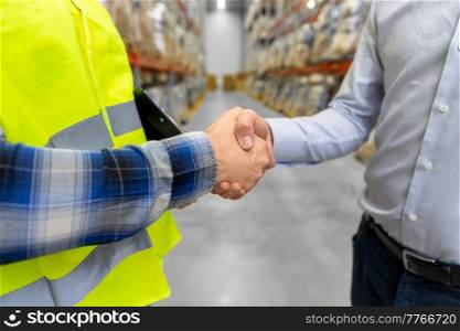 logistic business and cooperation concept - close up of manual worker and businessman shaking hands and making deal at warehouse. worker and businessman shaking hands at warehouse