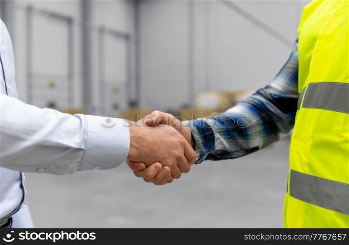 logistic business and cooperation concept - close up of manual worker and businessman with clipboard shaking hands and making deal at warehouse. worker and businessman with clipboard at warehouse