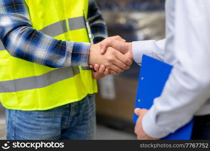 logistic business and cooperation concept - close up of manual worker and businessman with clipboard shaking hands and making deal at warehouse. worker and businessman shaking hands at warehouse