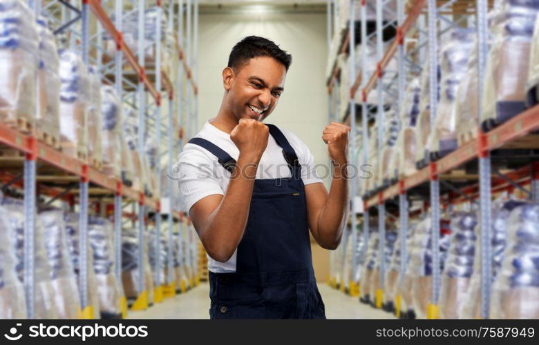 logistic business and people concept - happy smiling indian loader or worker celebrating success over warehouse background. indian worker celebrating success at warehouse