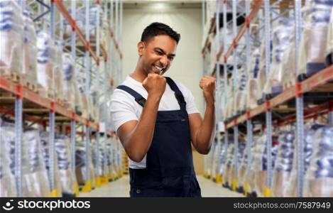 logistic business and people concept - happy smiling indian loader or worker celebrating success over warehouse background. indian worker celebrating success at warehouse