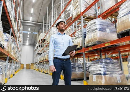 logistic business, shipment and people concept - businessman in helmet with clipboard checking goods at warehouse. businessman in helmet with clipboard at warehouse. businessman in helmet with clipboard at warehouse