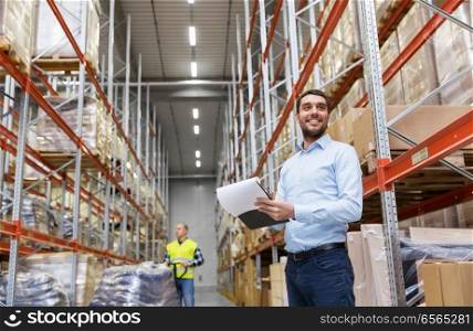 logistic business, shipment and people concept - happy businessman or manager with clipboard and loader at warehouse. happy businessman with clipboard at warehouse