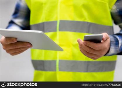 logistic business, technology, shipment and people concept - close up of man or manual worker with smartphone and tablet pc at warehouse. worker with phone and tablet pc at warehouse