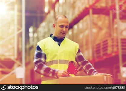 logistic, delivery, shipment, people and export concept - happy man in safety vest packing box or parcel with scotch tape at warehouse or mail storage