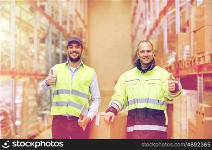 logistic, delivery, shipment, people and export concept - happy men or manual workers with boxes showing thumbs up at warehouse