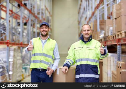 logistic, delivery, shipment, people and export concept - happy men or manual workers with boxes showing thumbs up at warehouse