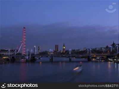 london eye with parliament and big ben behind river thames with boat at night seen from waterloo bridge