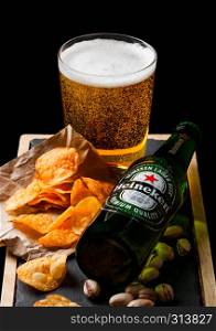 LONDON, UK - SEPTEMBER 26, 2018: Bottle of Heineken beer with glass and snack ostone board on black. Pistachios and pretzel and chips
