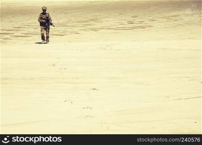 Lone army soldier in uniform, with service carbine in hands walking through hot sands desaturated, sepia tone. Military intervention or campaign in Middle East region, armed conflict in desert area. Infantry army soldier walking through hot desert
