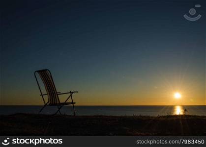 Lone chair by the setting sun at the horizon over the sea