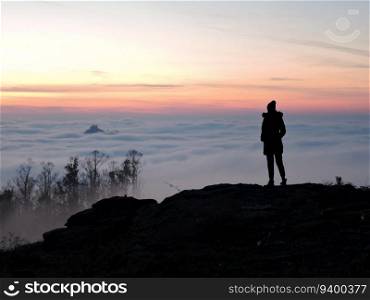 Lone female hiker contemplating the clouds from the top of a mountain