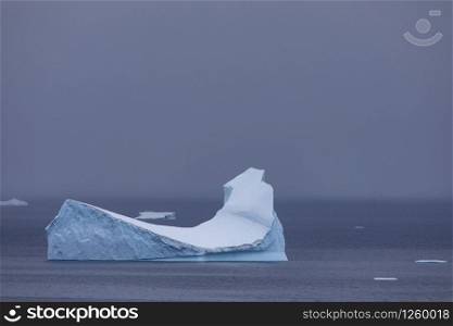 Lone iceberg shimmering blue swims in calm sea alone in Antarctica