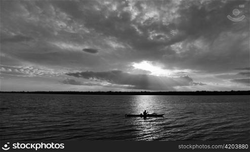 Lone kayak silhouetted on scenic lake at sunset.