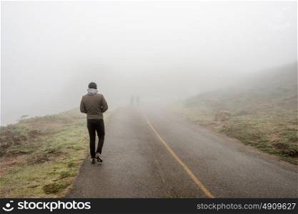 Lone man walking along the road through white fog