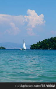 Lone sailboat approaching peaceful paradise island on turquoise sea. Lone sailboat