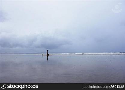 Lone surfer sitting on surfboard in shallow water, side view