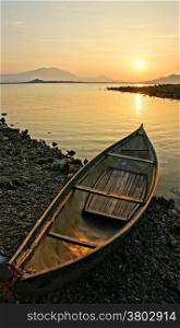 Lonely boat looking toward the sun, sunrise at horizon with yellow sky, boat on stone shore, calm, beautiful sightseeing in morning at sea